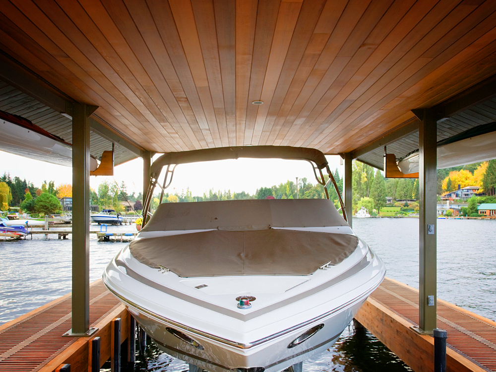Boat is parked under a awning, dock and ceiling have stained wood surfaces